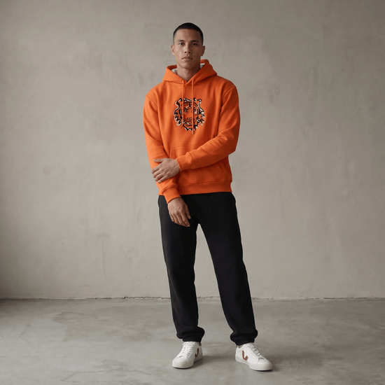Model wearing a Squatchfuzz Tiger Hoodie in vibrant orange with a tiger design, paired with black pants.